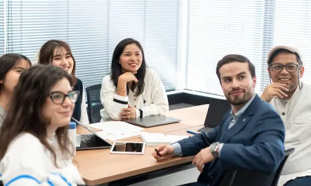 A diverse group of business students sitting around a conference table, smiling and participating in a group workshop.